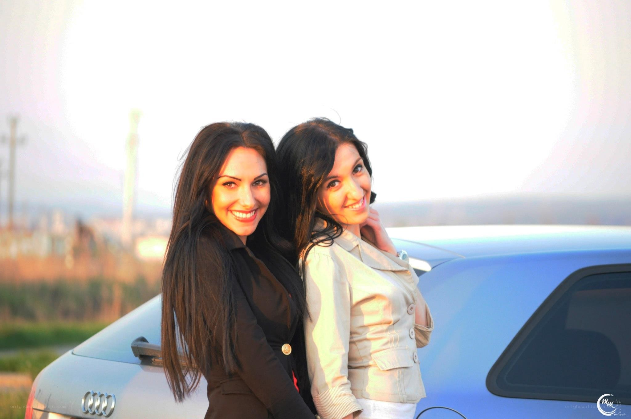 two women posing by a car