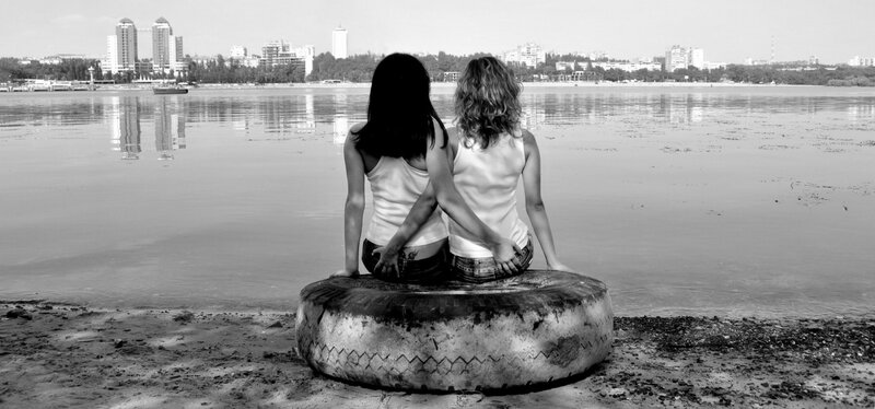Two women sitting on tire by water
