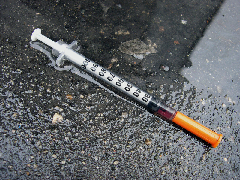 Used syringe on wet pavement
