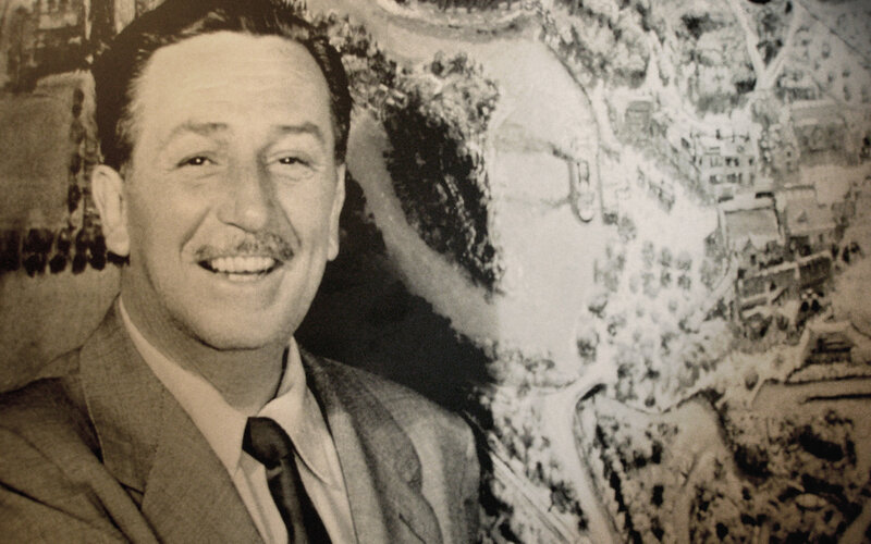 Walt Disney smiling in front of artwork