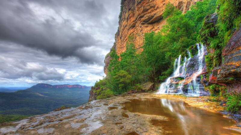 Waterfall on Cliff Face — Green, Dramatic, Photograph, Trees, Clouds, Brown