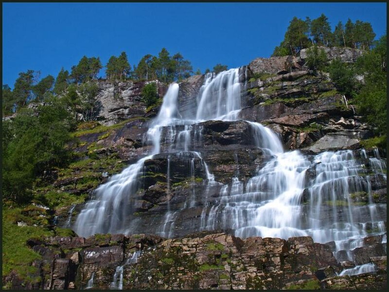 Waterfall on Rocky Cliff — Blue, Serene, Afternoon, Photograph, Trees, Rocks, Sky