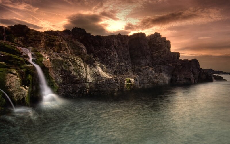 Waterfall on Rocky Cliff — Orange, Dramatic, Sunset, Photograph, Sea, Sky, Brown, Green