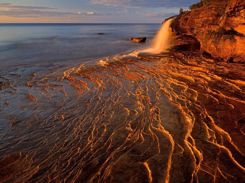 Waterfall on rocky shore at sunset