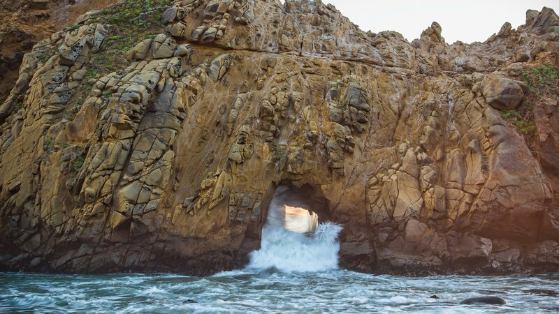 Wave Crashing Through Rock Arch — Brown, Dramatic
