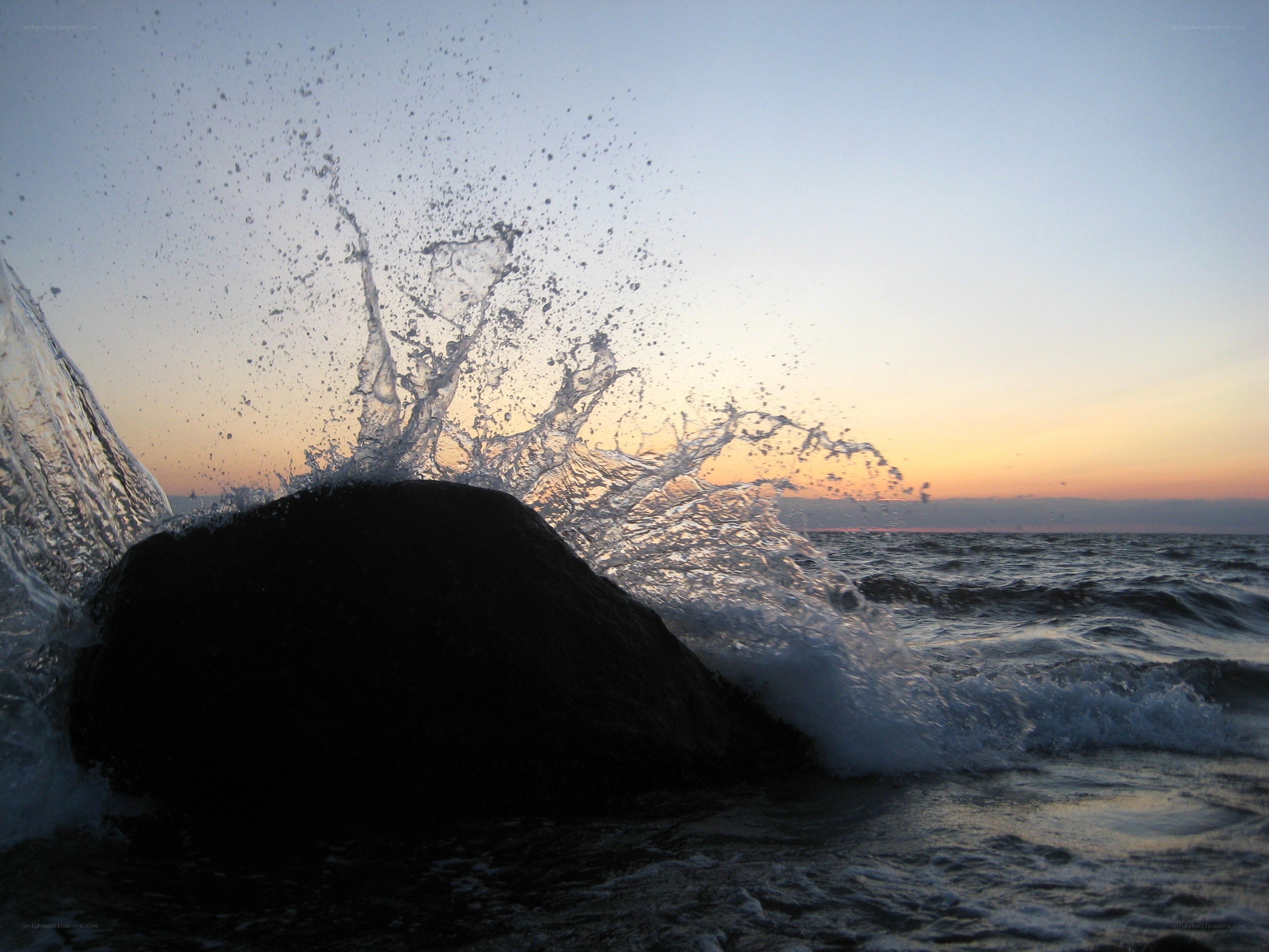 Wave splashing on rock at sunset