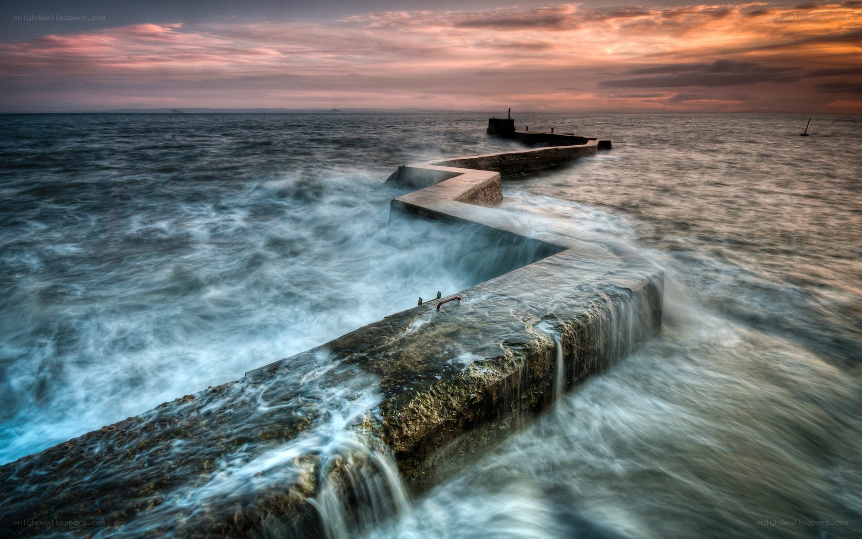Waves crashing on a pier at sunset