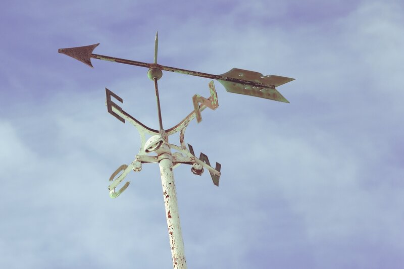 Weather vane against cloudy sky