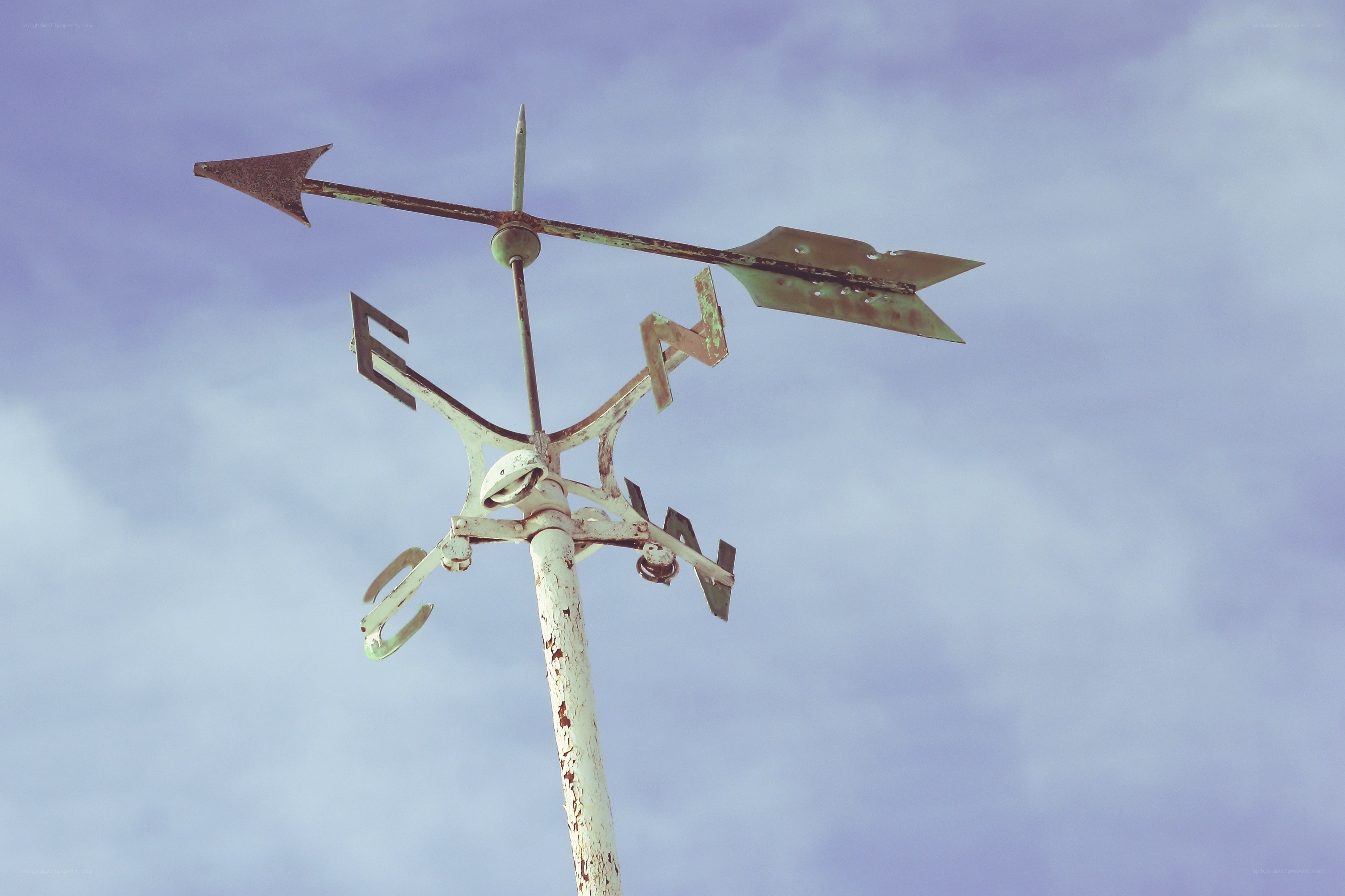 Weather vane against cloudy sky
