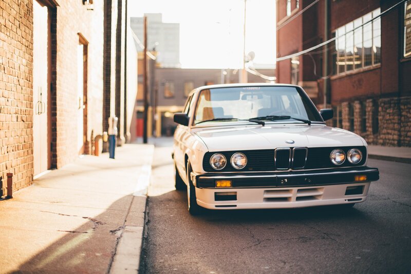 White BMW Sedan — Serene, Afternoon, Photograph, Brick Buildings
