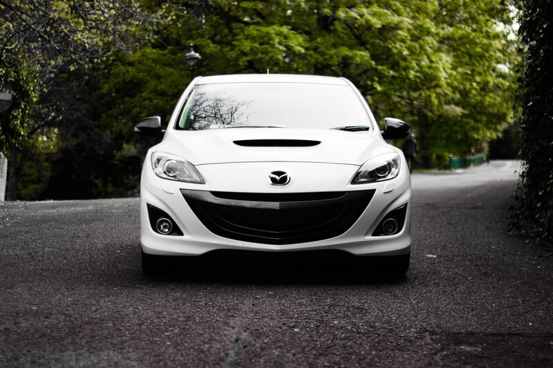 White Mazda on a tree-lined road