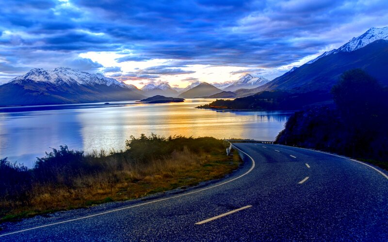 Winding Road by Lake — Blue, Dramatic, Sunset, Photograph, Mountains, Sky