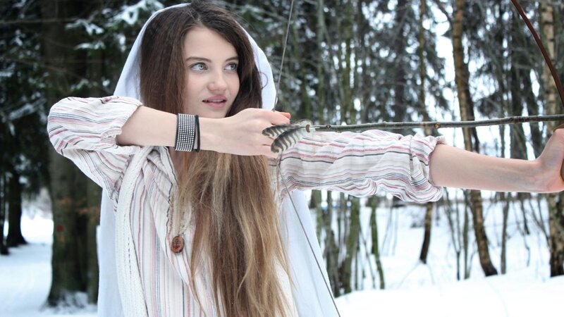 Woman aiming bow in snowy forest