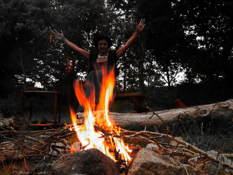Woman at campfire with arms raised