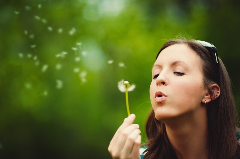 woman blowing dandelion seeds