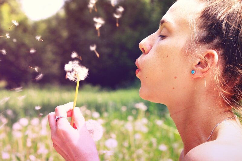 woman blowing dandelion seeds