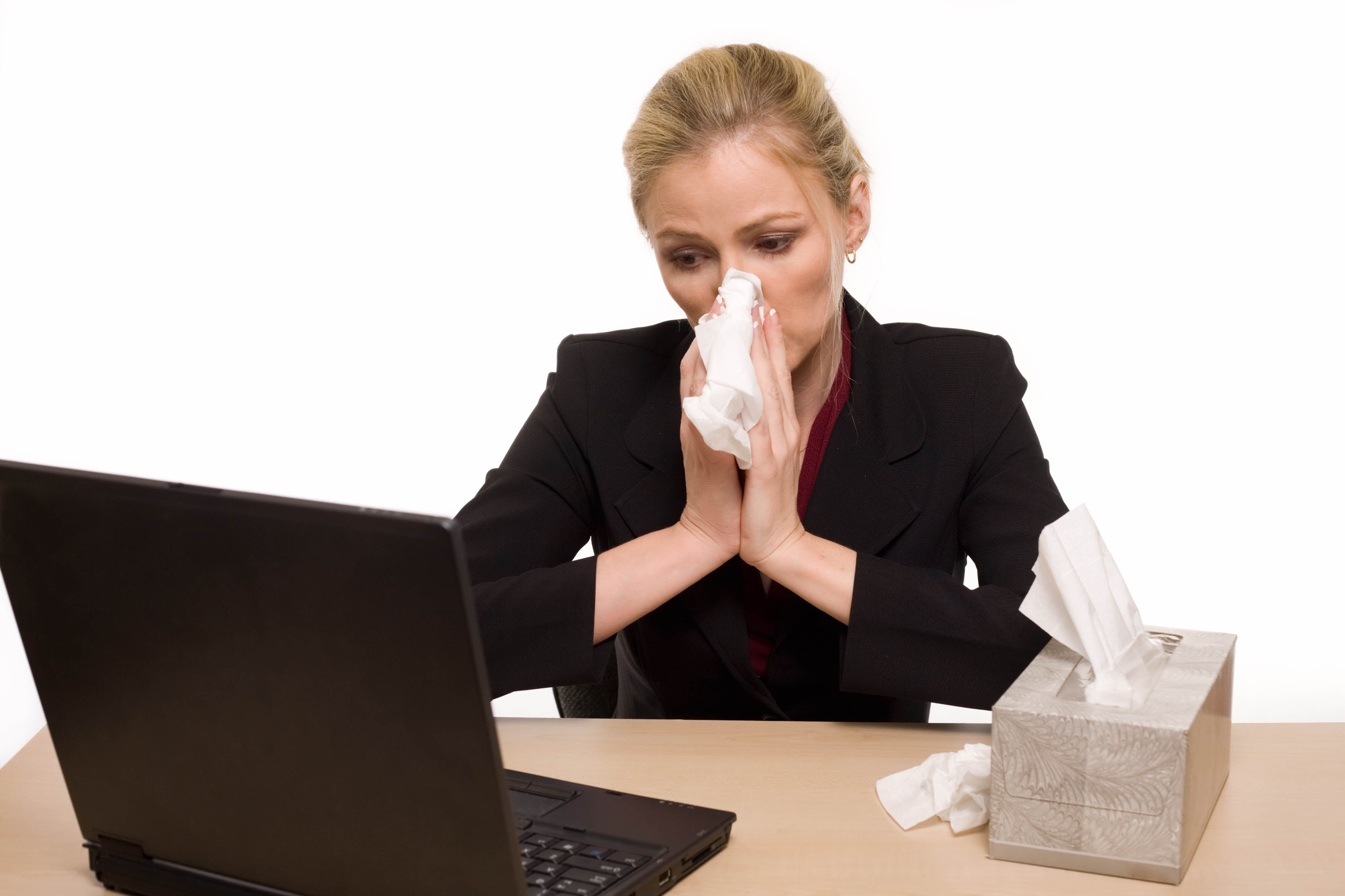 woman blowing nose at desk