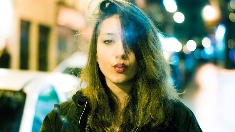 woman blowing smoke on city street