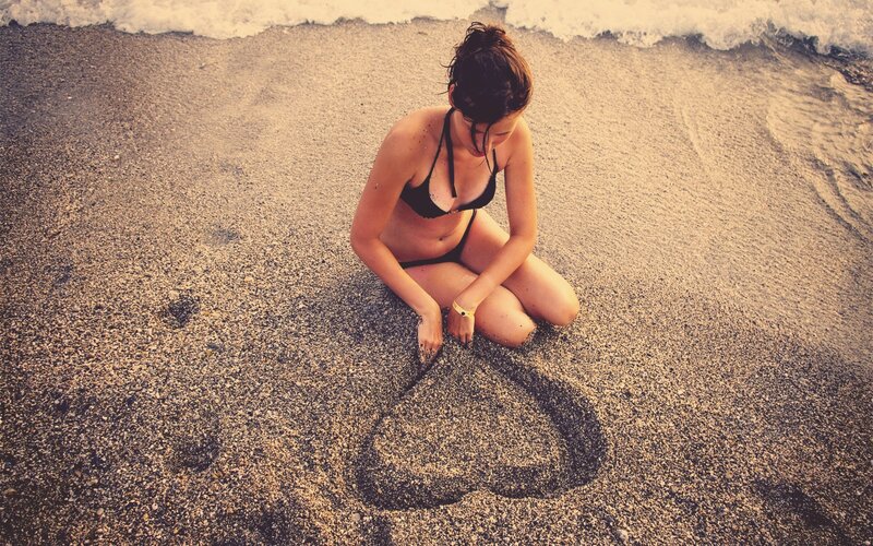 woman drawing heart in sand