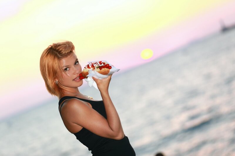 Woman eating hot dog at sunset