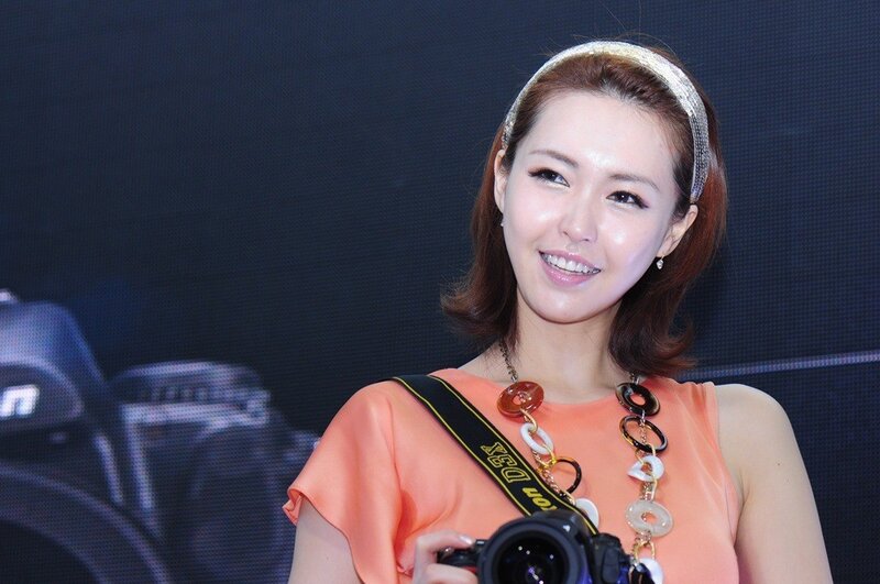 Woman Holding Camera — Orange, Smiling