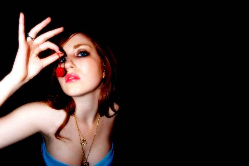 woman holding cherry near eye