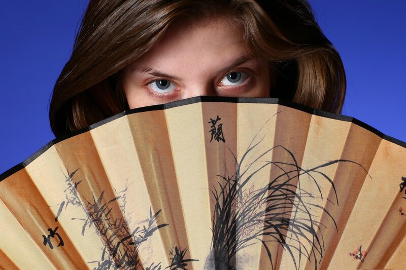 woman holding fan over face