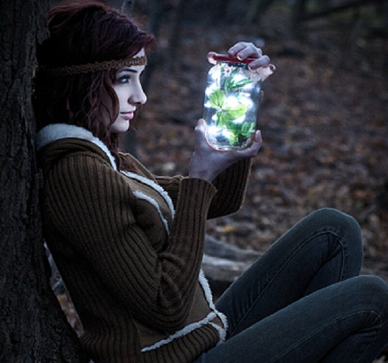 woman holding glowing jar in forest