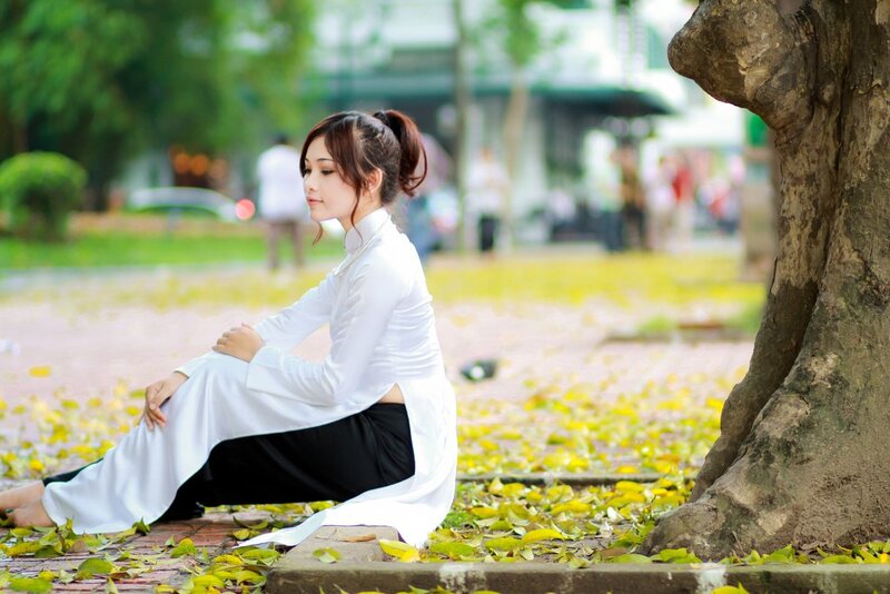 Woman in ao dai sitting by tree