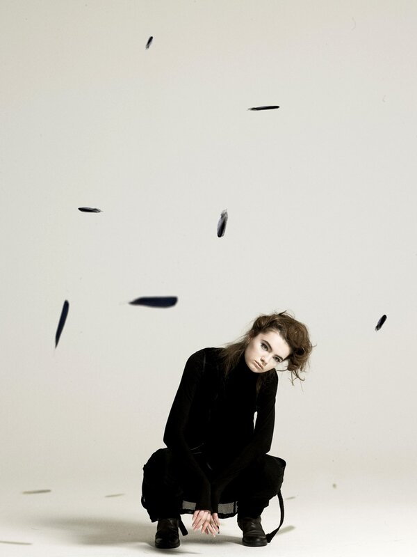 woman in black crouching with feathers