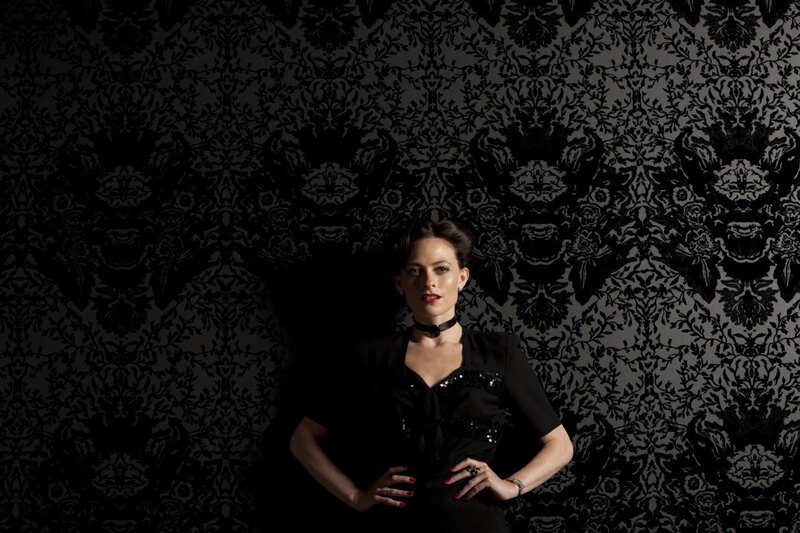 woman in black dress against patterned wall