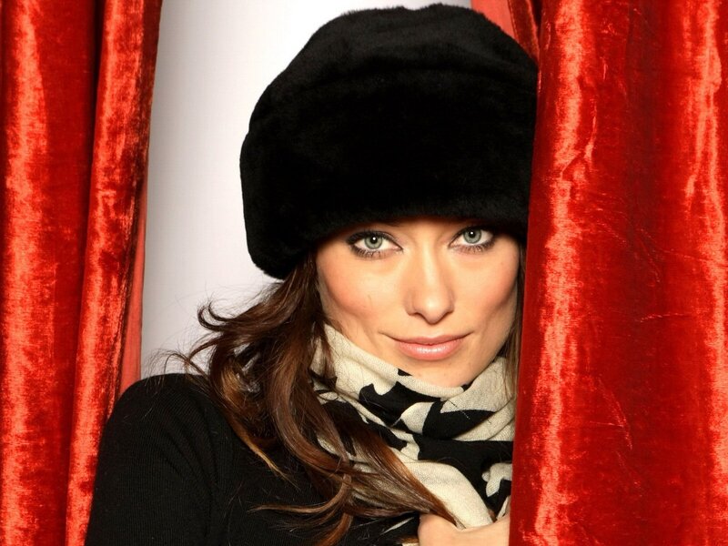 woman in black hat behind red curtain