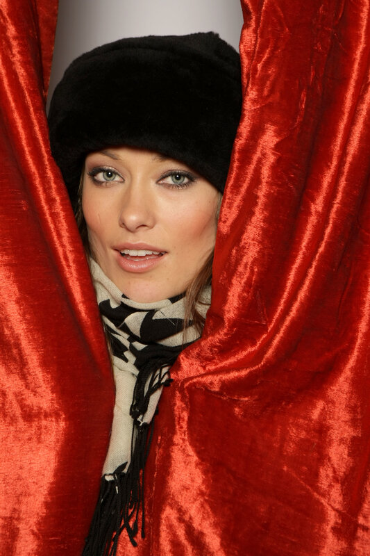 woman in black hat behind red curtain