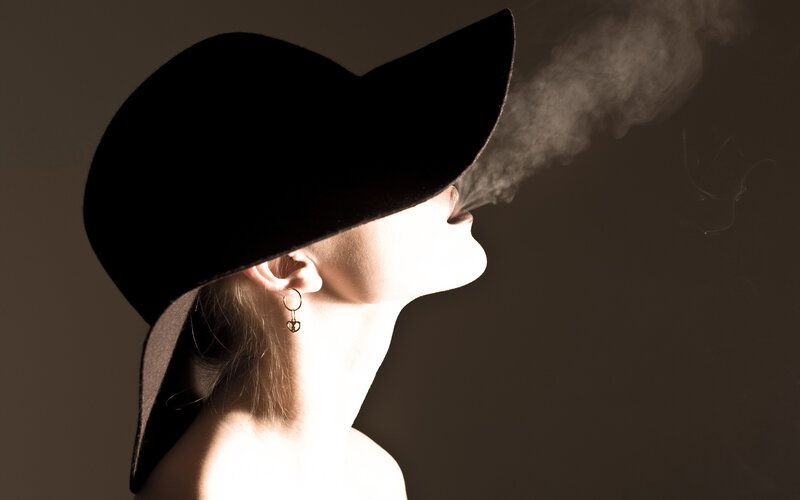 woman in black hat exhaling smoke