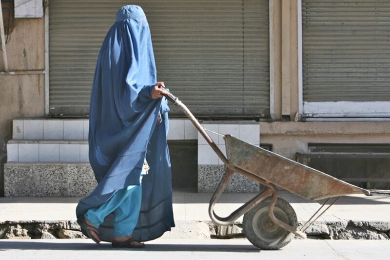 Woman in blue burqa pushing wheelbarrow