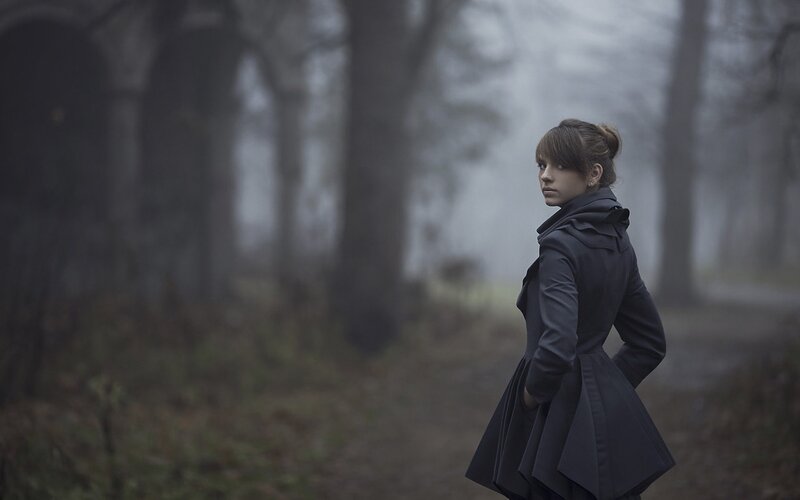 woman in dark coat in foggy forest