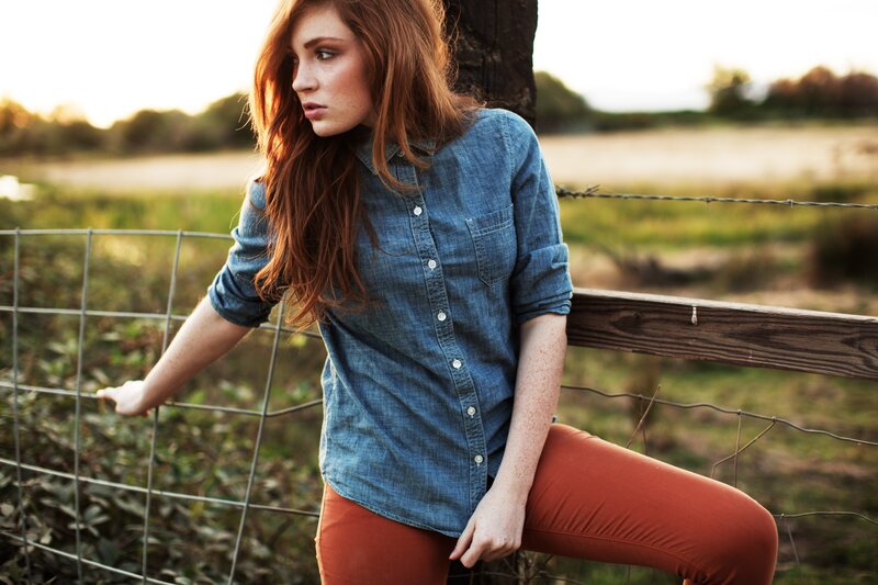 woman in denim shirt by fence