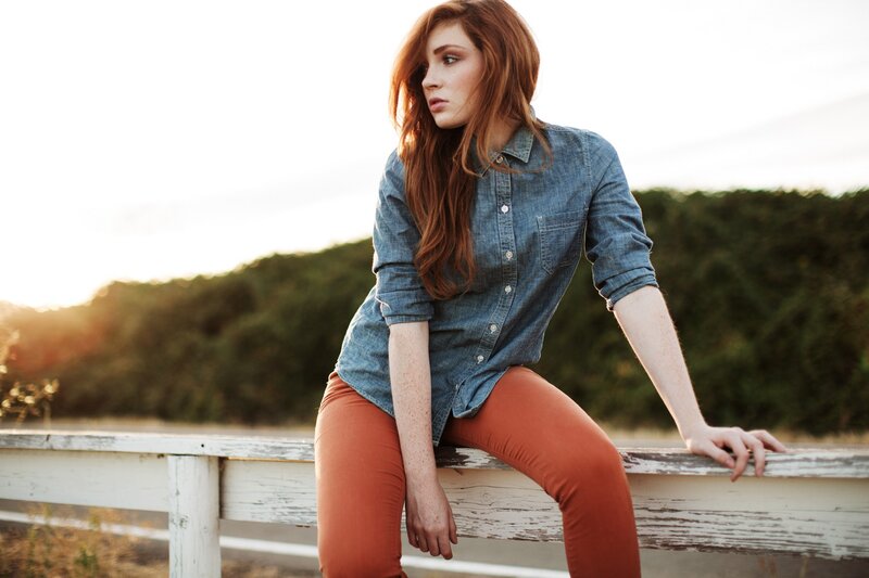 woman in denim shirt sitting on fence