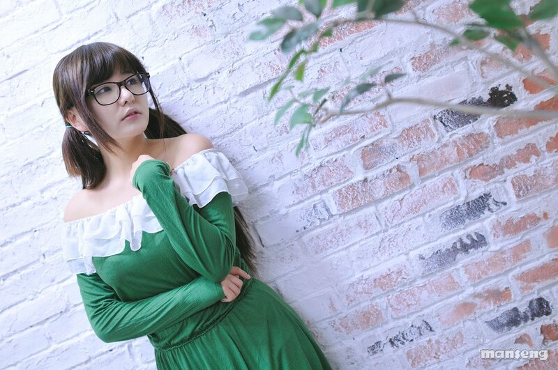 woman in green dress leaning on brick wall
