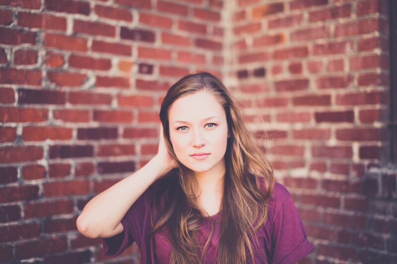 woman in purple shirt against brick wall