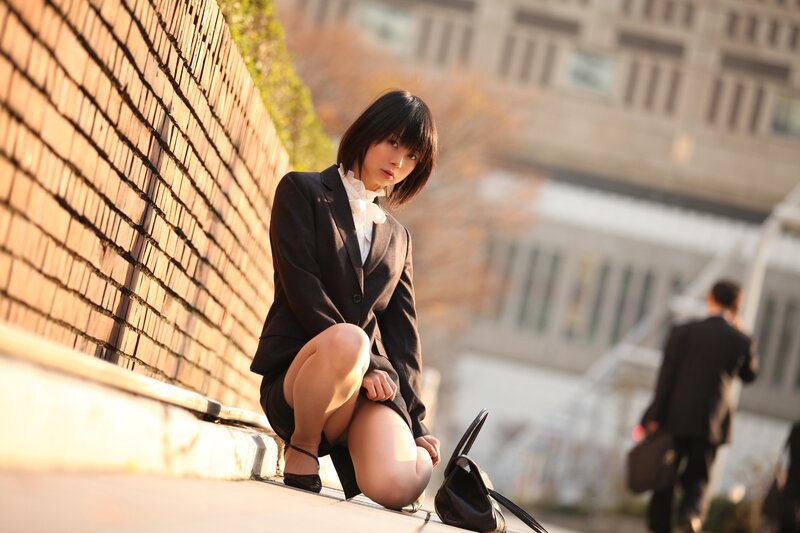 Woman in suit crouching by wall