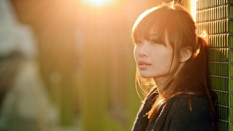 woman in sunlight by green wall
