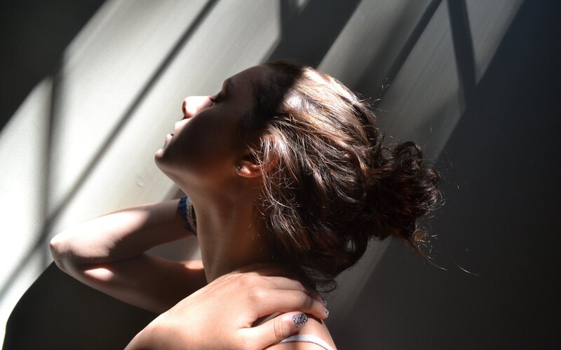 woman in sunlight with hands on neck
