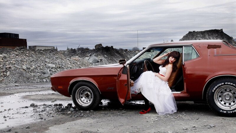 Woman in wedding dress by classic car