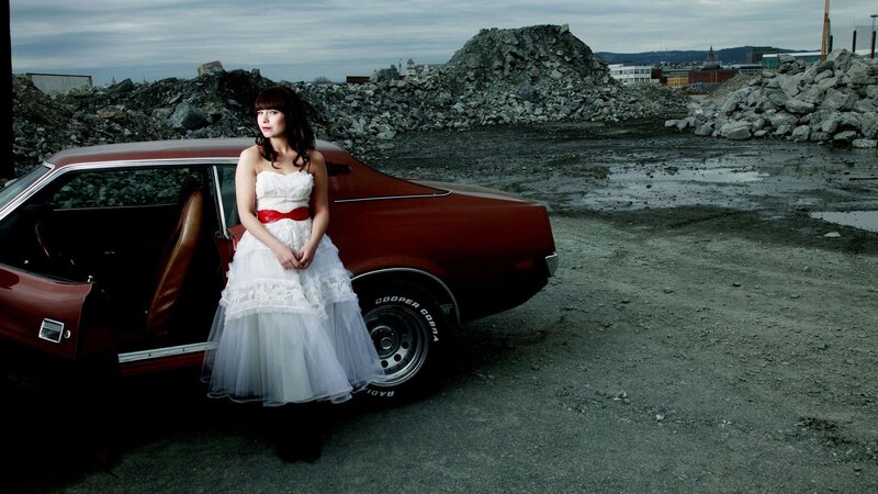 Woman in wedding dress by red car