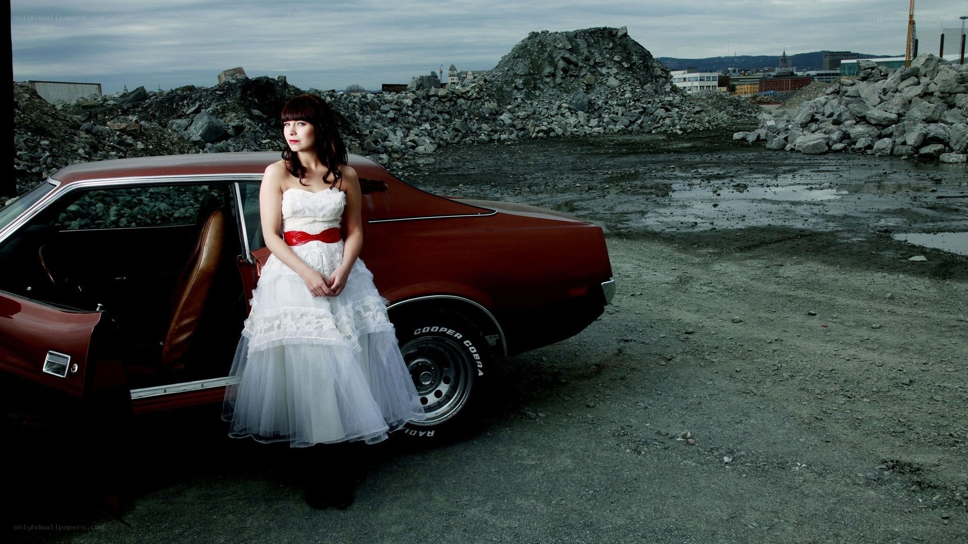 Woman in wedding dress by red car