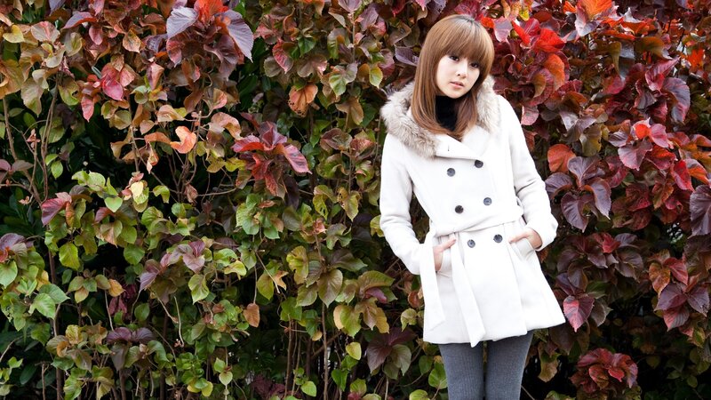 woman in white coat by foliage