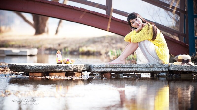 Woman in yellow sweater by bridge
