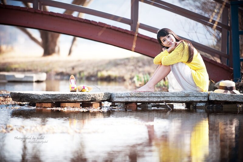Woman in yellow sweater by bridge