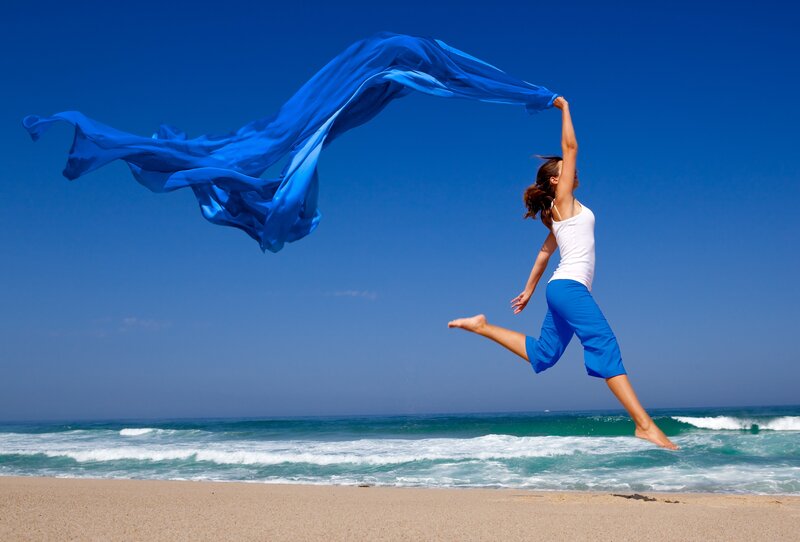 Woman jumping on beach with scarf